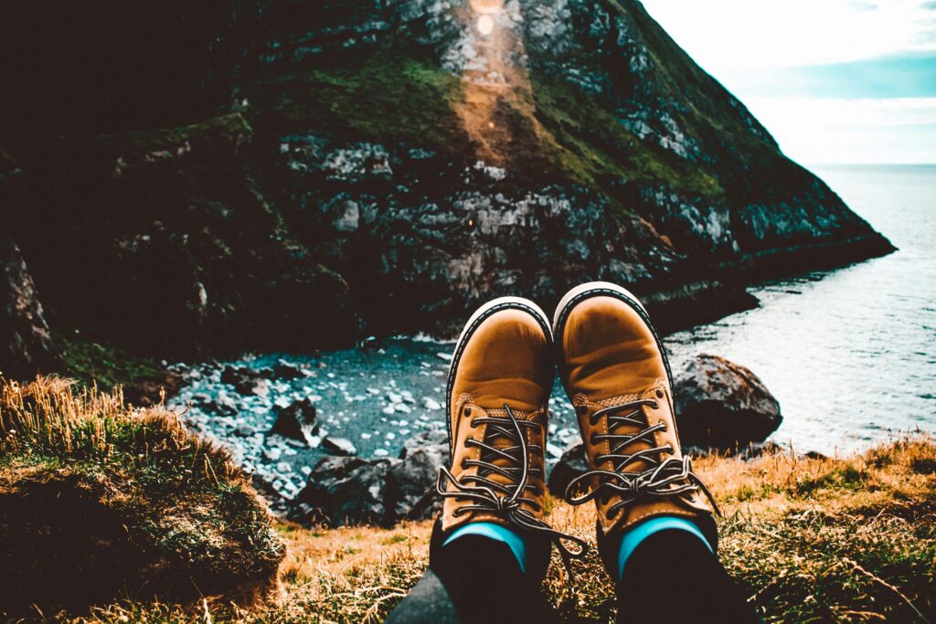 A person relaxes in hiking boots overlooking stunning coastal cliffs and ocean view.